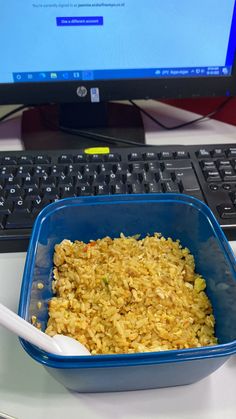 a blue bowl filled with rice next to a keyboard and computer monitor on a desk