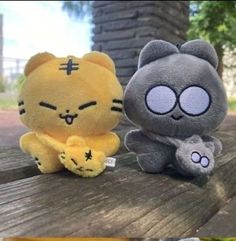 two small stuffed animals sitting on top of a wooden bench next to each other,