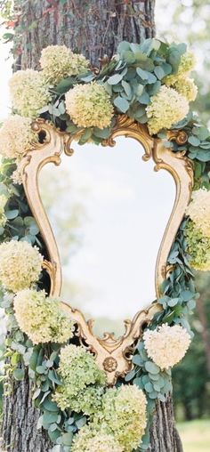 a mirror hanging on the side of a tree covered in flowers and greenery next to a forest