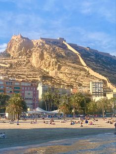 people are on the beach in front of some buildings and a large mountain behind them