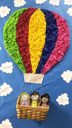 a colorful hot air balloon with three people in it and clouds on the wall behind it