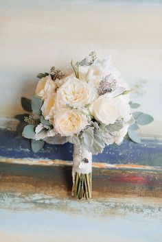 a bridal bouquet with white flowers and greenery sits on an old wooden surface