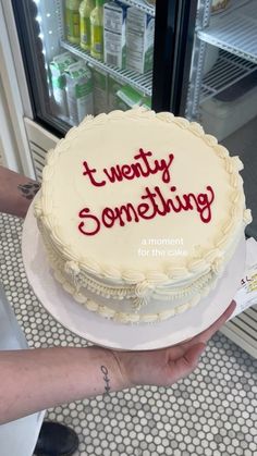 a cake with the words twenty something on it is being held by a woman in front of an open refrigerator