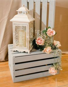 a white lantern sitting on top of a wooden crate filled with flowers and baby's breath