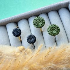 four green and black buttons sitting on top of a white cushion next to some feathers