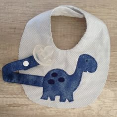 a baby bib with a blue dinosaur design on the front and white back, hanging from a hook