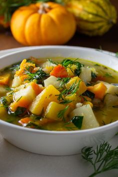 a white bowl filled with vegetable soup on top of a table next to pumpkins