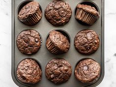 twelve chocolate muffins in a baking pan on a marble counter top, ready to be eaten