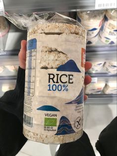 a person holding up a can of rice in a grocery store with other items behind them