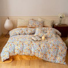 a bed with yellow and blue flowers on it, next to a table with a candle