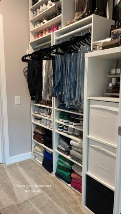 an organized closet with white shelving and lots of clothes on hangers in it