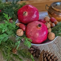 two pomegranates in a white bowl surrounded by pine cones and nuts