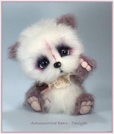 a small stuffed animal with white fur and purple eyes sitting on a gray background,