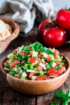 a wooden bowl filled with chopped vegetables on top of a table next to bread and tomatoes