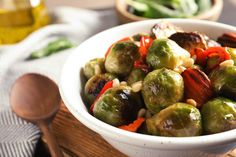 a white bowl filled with brussel sprouts and carrots next to a wooden spoon