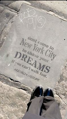 someone is standing in front of a sign that says new york city and dreams on the sidewalk