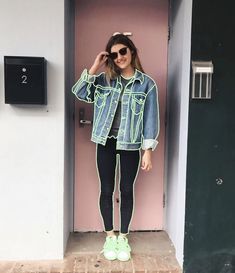 a woman standing in front of a pink door wearing green shoes and a denim jacket