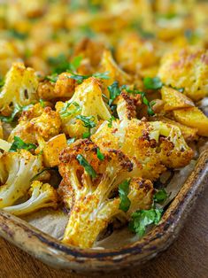 roasted cauliflower with parsley and herbs in a baking dish on a wooden table