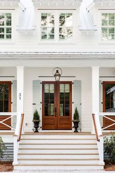 a white house with two brown doors and steps leading up to the front door that has potted plants on either side