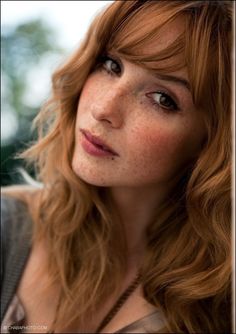 a woman with red hair and freckles looks into the distance while posing for a photo