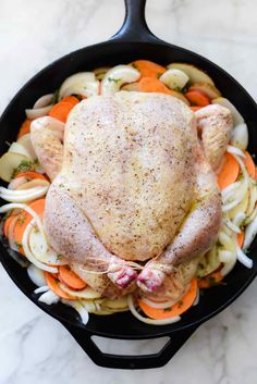 a whole chicken in a skillet with carrots and onions