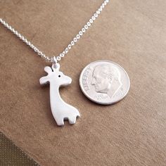 "My Tiny Giraffe Necklace is handmade using fine silver and my original giraffe design. She has a soft, brushed finish and the back is stamped with my dragonfly maker's mark and \".999\" to signify fine silver. Your choice of sterling silver chain is included. The model photo is for size reference. She's wearing a giraffe of the same size on a 16\" round cable chain. S I Z E : About 1\" tall (25 mm) including the ring. A V A I L A B I L I T Y : Made-to-order, ships 1-2 weeks after purchase unles Silver Animal Design Jewelry For Gifts, Silver Jewelry With Animal Design For Gift, Giraffe Design, Giraffe Necklace, A Giraffe, Mom Necklace, Maker's Mark, Pretty Gift, Silver Flowers