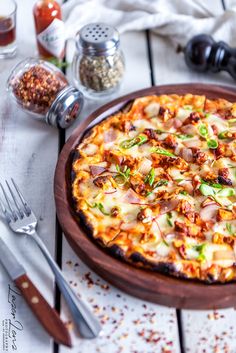 a pizza sitting on top of a wooden plate next to silverware and utensils