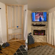 a living room with a fireplace and television in the corner, surrounded by white curtains