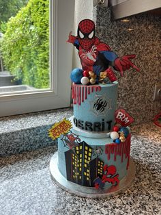 a three tiered cake decorated with spiderman and other decorations on top of a counter