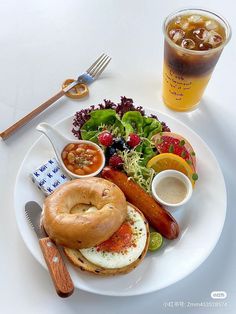 a white plate topped with a bagel, fruit and salad next to a drink