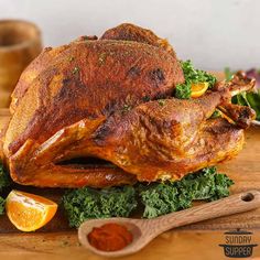 a roasted turkey with kale and oranges on a cutting board