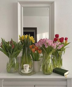 several vases filled with tulips and other flowers on top of a dresser