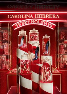 a display case filled with red and white candy canes in glass jars next to a neon sign that reads carolina herbera sweet holidays