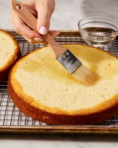 a person holding a brush over a cake on a cooling rack next to two slices of bread