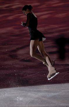 a female figure skating on the ice in a black dress and white shoes with her legs spread out