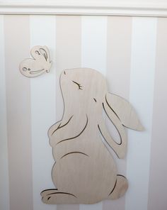 a wooden cutout of a rabbit sitting on the ground next to a striped wall