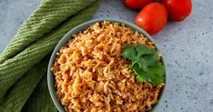 a bowl filled with rice next to tomatoes and a green towel on the table top