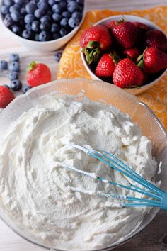 a bowl filled with whipped cream next to blueberries and strawberries on a table