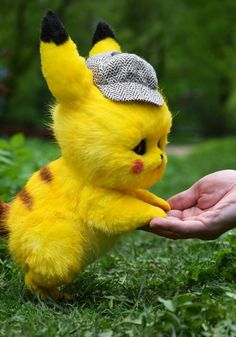 a person holding a small yellow stuffed animal in their hand with grass and trees in the background