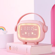 a pink alarm clock sitting on top of a stack of books next to a rainbow