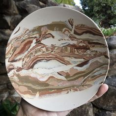 a hand holding up a white and brown marbled ceramic bowl in front of a stone wall