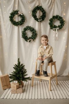 a little boy sitting on a chair in front of christmas decorations