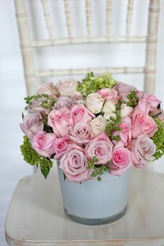 a bouquet of pink roses in a blue vase on a white chair with greenery