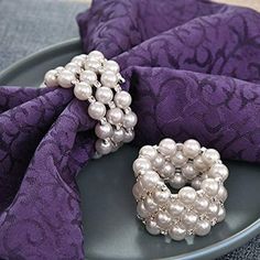 a plate topped with two napkin rings and pearls on top of purple cloth covered placemats