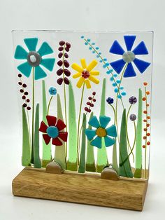 a glass block with flowers and grass in it on a wooden stand against a white background