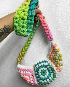 a hand holding a multicolored crocheted bag on top of a white wall