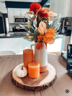 an arrangement of flowers and candles on a wood slice in a kitchen area with white cabinets