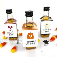 three halloween themed bottles with labels on them and candy candies scattered around the bottle