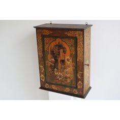 an ornate wooden cabinet with paintings on the front and side panels, hanging from a white wall