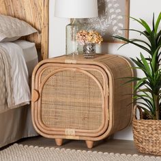 a wicker side table next to a bed with a lamp and plants on top